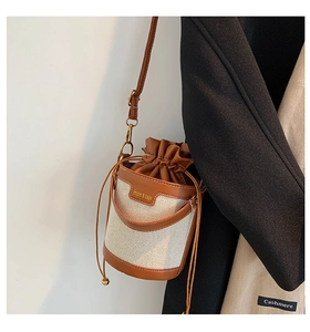 Detail of canvas bucket bag with brown leather trim and golden logo on white wall background