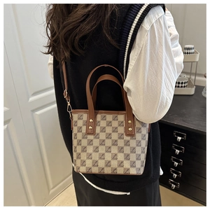Detail of checkered canvas tote bag with leather straps and gold studs on a model