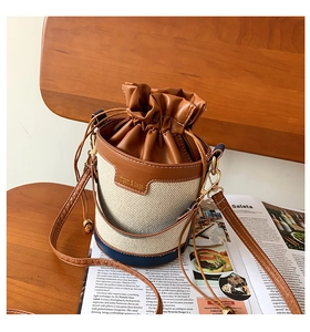 Detail of canvas bucket bag with contrast leather trim and drawstring on a wooden chair