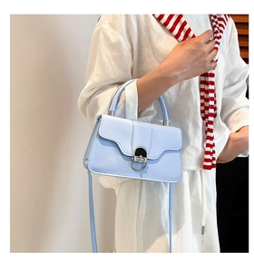 Close-up of light blue flap shoulder bag featuring a round silver metal buckle
