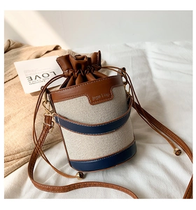 Detailed macro view of woven cream bucket bag with brown leather trim and navy contrast band