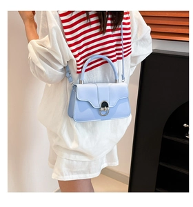 Detail of light blue crossbody bag featuring a curved flap and silver metal ring buckle