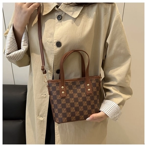 Detail of checkered shoulder bag with dual handles and gold hardware on beige coat