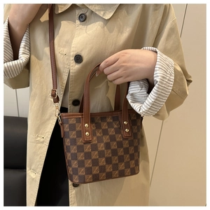 Detail of checkered bucket bag with leather handle and golden hardware on trench coat