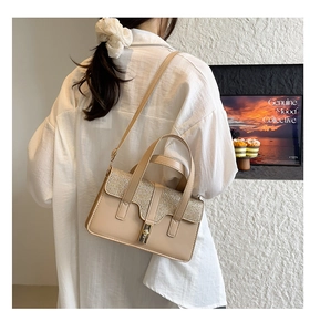 Detail of beige handbag featuring sequin stitching, golden turn-lock, and round handle