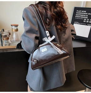 Dettaglio della borsa sottobraccio in pelle marrone scuro con fiocco in pizzo e placca