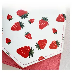 Detailed close-up of white leather with red strawberry print and pink stitching on the bag