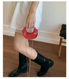 Red pleated acrylic dumpling bag with gold chain strap shown being held by a model