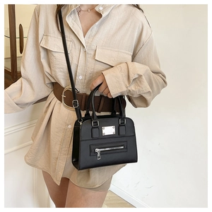 Detail view of black small square bag with silver metal plaque and adjustable strap