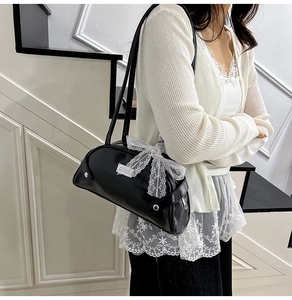 Dettaglio della borsa bowling in pelle nera con fiocco in pizzo bianco e doppi manici