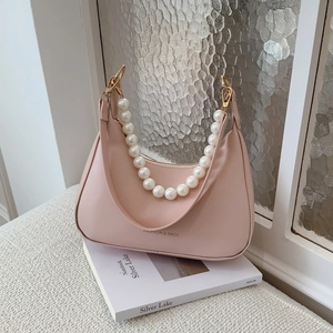 Pink hobo handbag with large pearl strap and gold hardware on white book display