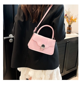 Detailed view of pink leather handbag featuring a round silver metal lock and flap closure