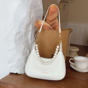 White hobo shoulder bag with large pearl chain and adjustable strap on a wooden table