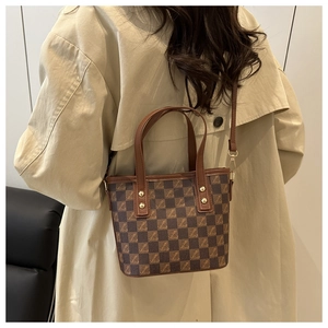 Close-up of a brown checkered bucket bag with letter patterns and golden rivets
