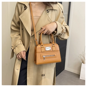 Caramel leather Boston bag shown on model with shoulder strap and metal plate detail