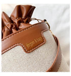 Detail of drawstring bucket bag with beige canvas, brown leather trim and metal hardware