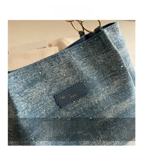 Detail of light blue denim tote with silver rhinestones and gold metal ring handle