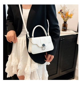 Detail of white leather shoulder bag featuring a prominent silver round buckle and top handle