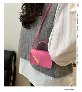 Pink leather crossbody square bag with gold metal trim worn over a grey vest