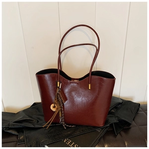 Detail of burgundy patent leather tote bag with metallic tassels on a dark leather coat