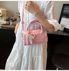 Pink Boston bag with pearl bow and lace detail shown on white dress in a cafe