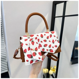 Detail of white strawberry print handbag with brown straps and golden metal hardware