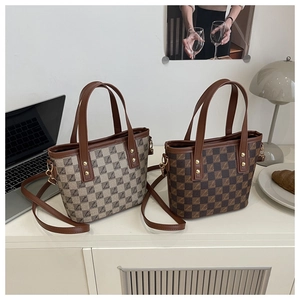 Detail of checkered tote bag with leather handle, gold rivets and adjustable strap