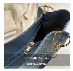 Close-up of blue denim tote bag with gold metal ring and smooth zipper detail