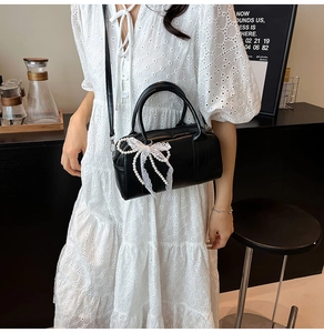 Close-up of black leather handbag with pearl bow decoration worn by a model