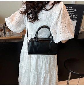 Modern black leather Boston bag worn cross-body with white lace dress outfit