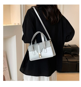 Silver sequin handbag shown on model featuring a gold twist lock and dual top handles