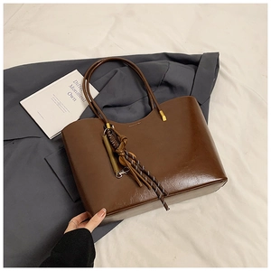 Detail of a dark brown glossy leather tote bag with a woven decorative charm