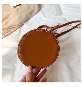 Detail of vintage brown cylindrical bag featuring white contrast stitching and gold ball charm