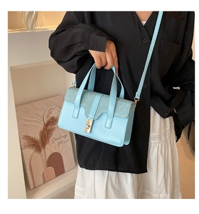 Detail of light blue crossbody bag featuring glitter texture flap and gold metal buckle
