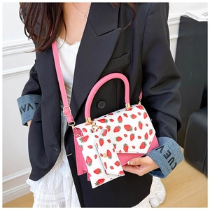 Detail of pink and white crossbody bag featuring strawberry prints and a mini charm pouch