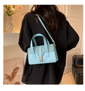 Detail of light blue crossbody bag with glitter flap and gold twist lock on a model