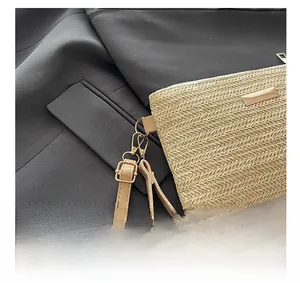 Detail showing the adjustable brown leather strap and gold hardware on the woven straw bag