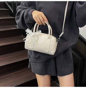 Detail of cream Boston bag with lace bow and pearl chain held on a wooden staircase