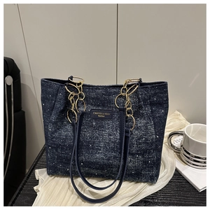 Detail of dark blue denim tote bag with star patterns and gold chain strap on desk