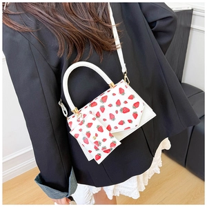 Detail of white crossbody bag with strawberry print and matching small coin purse pendant