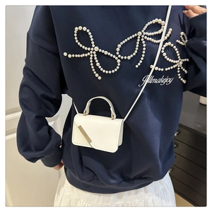 Detail showing white mini crossbody bag with gold metallic trim and thin leather strap