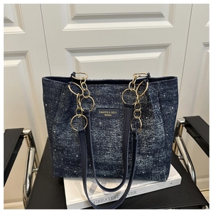 Close-up of a blue denim tote bag with white floral pattern and gold chain strap