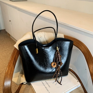 Minimalist black glossy tote bag with vintage pendant on chair in modern interior