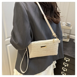 Detail of woven straw crossbody bag featuring golden zipper and herringbone texture