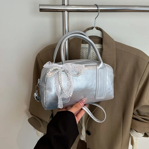 Silver metallic Boston handbag featuring lace bow and pearl details in hand-held pose