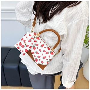 Detail view of white strawberry print tote bag with brown leather handles and gold clasp