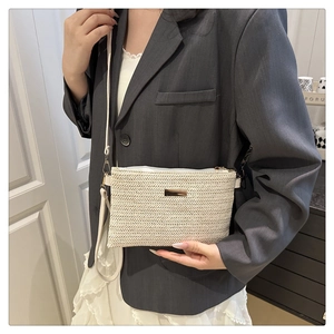 Close-up of minimalist straw crossbody bag with gold metal plaque on model outfit