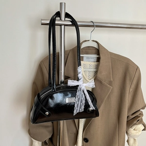 Borsa bowling in vernice nera con fiocco in pizzo bianco davanti a un blazer autunnale