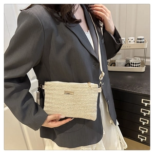 Close-up of cream woven crossbody bag featuring a golden metal logo plate and strap detail