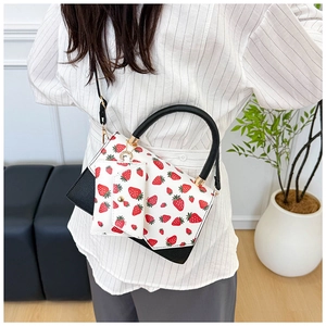 Detail of white crossbody bag with strawberry print and black contrast leather panels